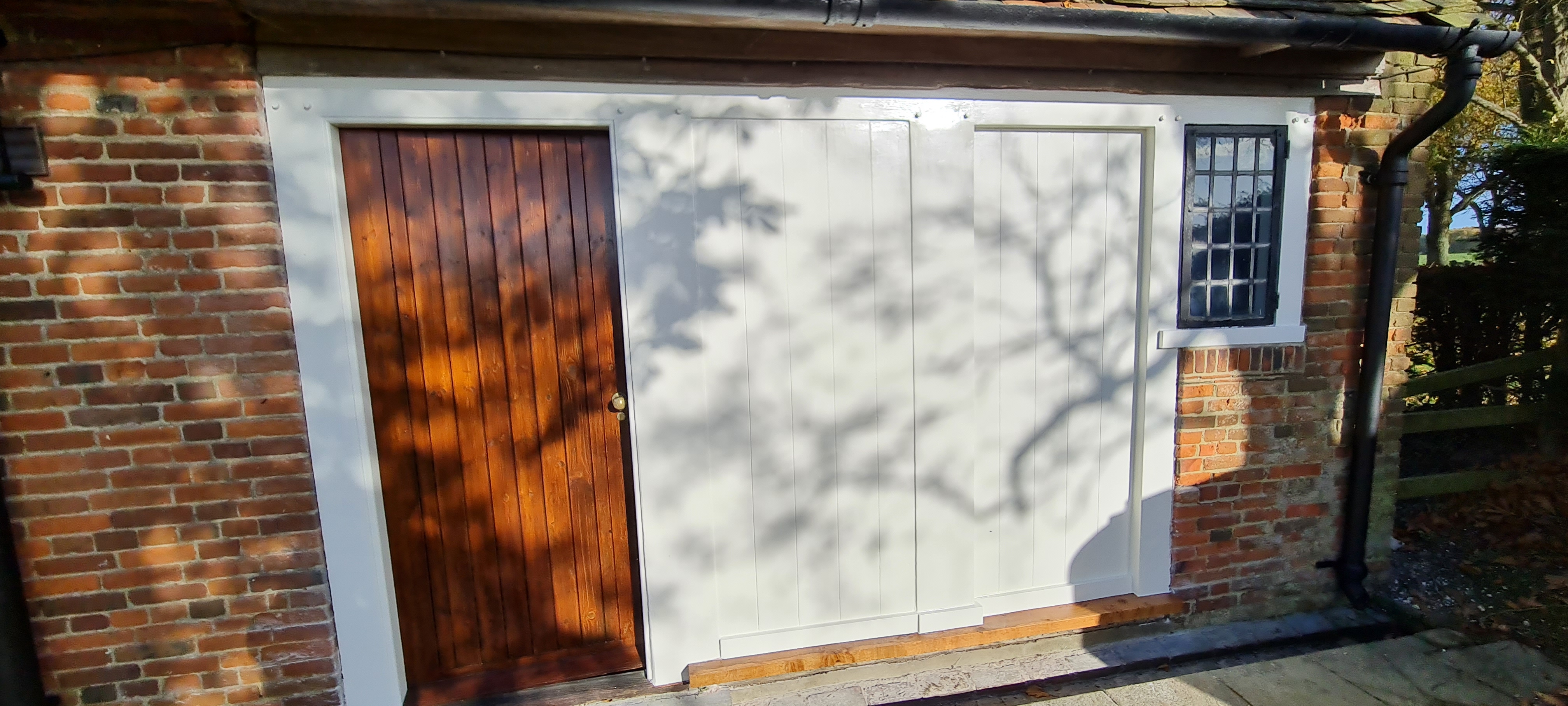Country outbuilding after painting — white doors and oiled timber door